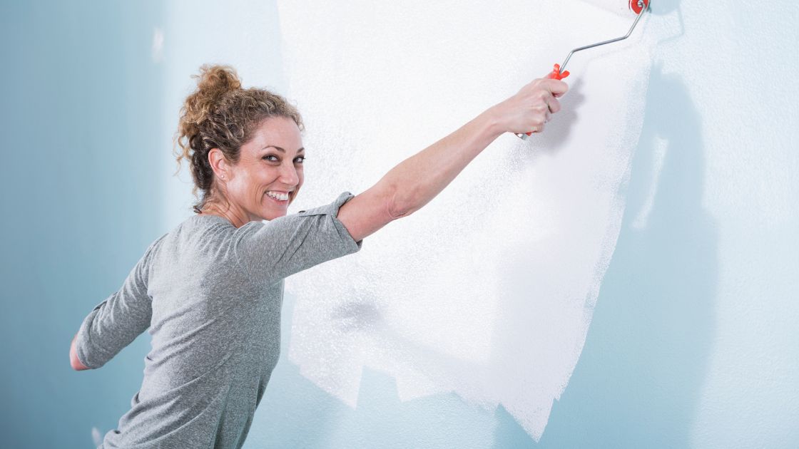 mujer sonríe mientras pinta de color azul pastel las paredes de su cocina