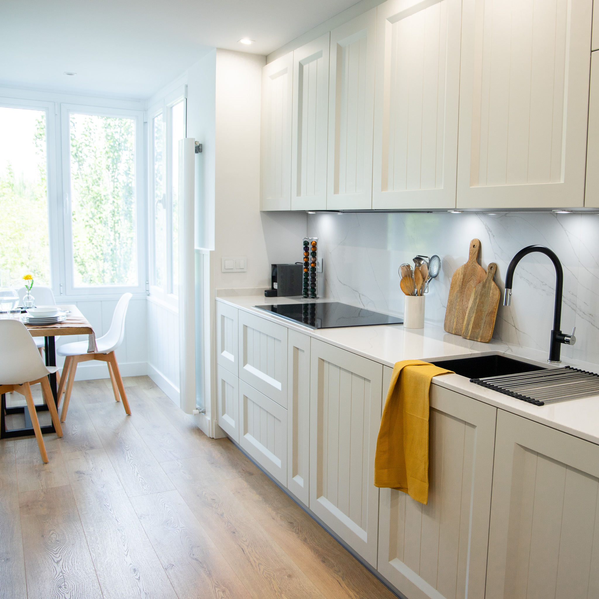 una cocina blanca con accesorios de madera y una iluminación natural única, esta cocina tiene una ventana que ofrece una vista directa a la naturaleza