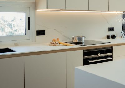 una cocina blanca con isla abierta al salón y la entrada