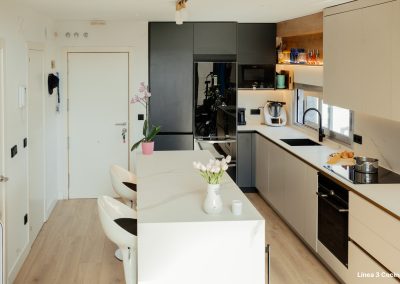 una cocina blanca con isla abierta al salón y la entrada