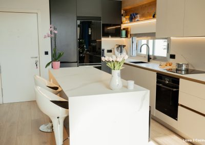 una cocina blanca con isla abierta al salón y la entrada