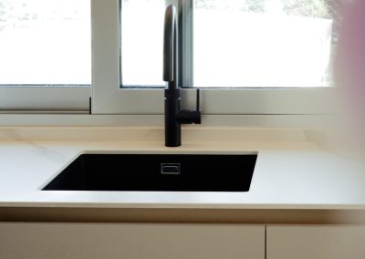 una cocina blanca con isla abierta al salón y la entrada